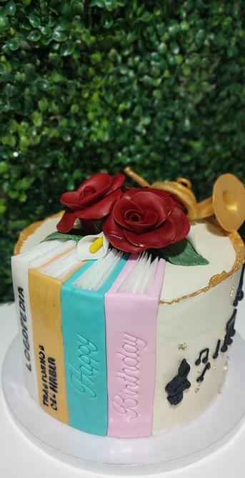 Parte delantera de la tarta en la que se pueden ver 4 libros de diferentes colores y unas flores encima