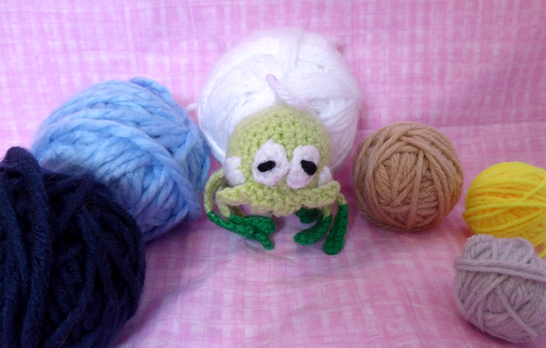 An amigurumi plush of the Pokémon Tarountula surrounded by various coloured balls of yarn.