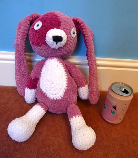 An amigurumi rabbit plush made with fluffy pink and white yarn and white button eyes.