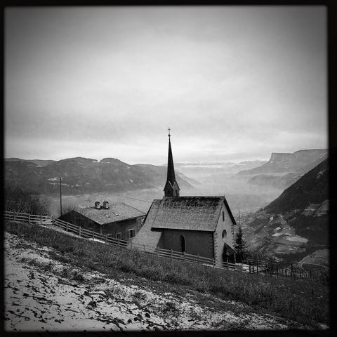 Una chiesetta e la vista verso le cime delle Dolomiti in lontananza con nebbia nel fondovalle