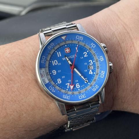 A watch featuring a bright blue dial, red GMT hand, combination timing/worldtimer internal bezel, and inner 24-hour ring with metal mesh strap. 