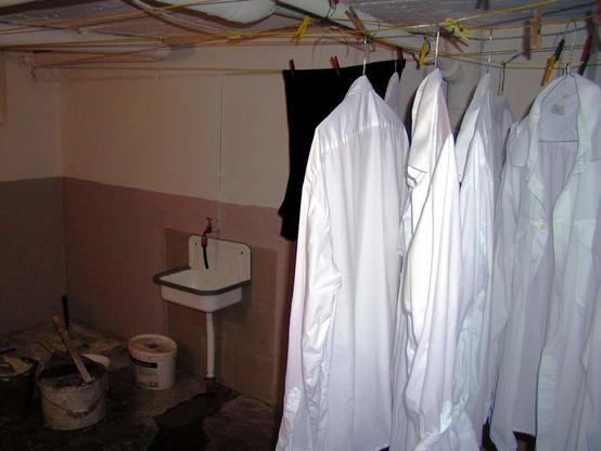 White shirts hanging to dry on clotheslines in a basement laundry room with a sink and paint buckets.