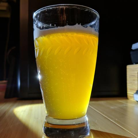 A square cropped photo of a partially full glass of wheat beer. It is a bit cloudy or hazy and a light amber or golden color. It is illuminated from behind and to the side to get a good representation of that actual color and clarity.