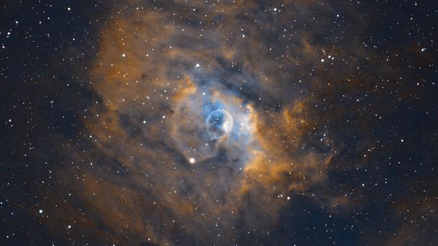 The Bubble Nebula (NGC 7635, Caldwell 11, Sharpless 162 etc etc)

Black background with some stars sprinkled throughout. Stars are mostly small to medium size and do not show much colour (just white).

The is a lot of orange nebulosity spread throughout. Nestled in the center is an area of blue nebulosity and a nearly circular white-edged bubble.