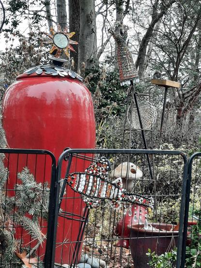 Red urn fountain in a garden surrounded by a beaded koi and a beaded mini dress form.  A beaded sunset star and solar light are on top of the fountsin.