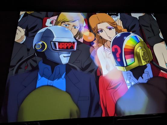 Photo of the part of the film with Daft Punks self characters at the award part of the movie with 'Happy' on Thomas helmet & '?' on Guy-Man's helmet. Yes you can see how the AI has made the original art quality much worse.