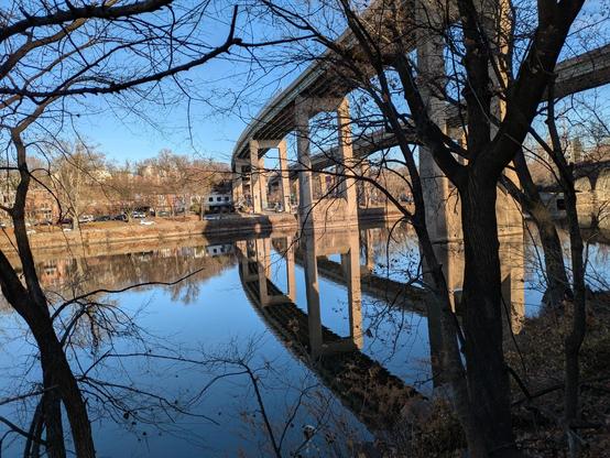 Photo it two curved concrete and steel bridges over a river and their reflections on the mirror-still water below.