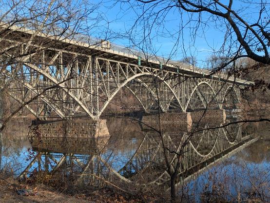 Photo of a late 19th century cast with its reflection iron bridge and it's reflection on the mirror-still surface of the river below it.