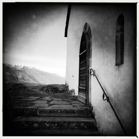 Le scale che conducono alla porta in legno della chiesetta con le cime innevate delle montagne sullo sfondo