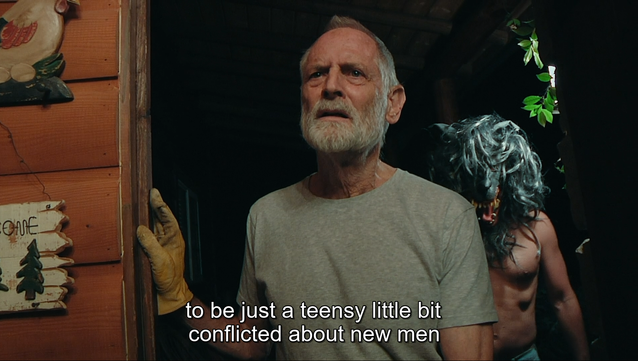 Screenshot from the final episode of "The Creep Tapes," in which we watch an elderly woman explain to her new lover that her son "gets a little conflicted about new men," as we see the son, a serial killer, hover in the background behind him, naked except for a menacing wolf's mask, getting prepared to kill the man.