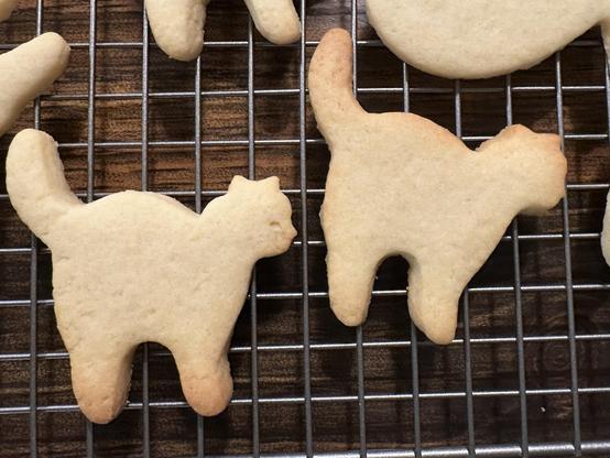 Sugar cookies cooling on a grid in the shape of the silhouette of cats standing in profile. Their little feet and tails are brown on the edges. 