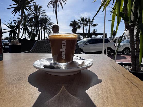 Photo of a corridor coffee sitting on a table with palm trees and sunshine behind. 