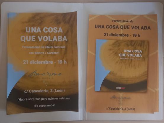 Fotografía a una carpeta abierta con dos tipos de carteles. En el cartel de la izquierda se ve la imagen de portada ampliada del álbum ilustrado ocupando todo el folio. Se lee: "Una cosa que volaba. Presentación de álbum ilustrado con Beatriz L Cardenal. 21 diciembre - 19h. Logo de Amarone Vinnería. Calle Cascaleria, 3 (León). Habrá sorpresa para quienes asistan. ¡Te esperamos!". En el cartel de la derecha, aparece la portada del libro en el centro de la imagen sobre un fondo de patrón de panal de abeja hexagonal. Se lee: "Presentación de Una cosa que volaba. 21 diciembre - 19h. Logo de Amarone Vinnería. Calle Cascalería, 3 (León)".