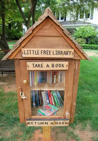 An outdoor cabinet with a roof and glass door. Within the cabinet are books on shelves.