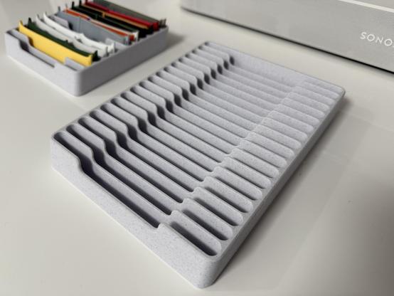 A close-up of an empty gray watch band organizer tray with clean, evenly spaced grooves designed to hold multiple watch straps. In the background, another tray neatly stores colorful watch bands, adding a touch of organization and style to the workspace.