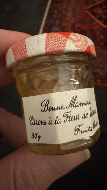 A hand holding a small jam jar containing a yellow jelly.
