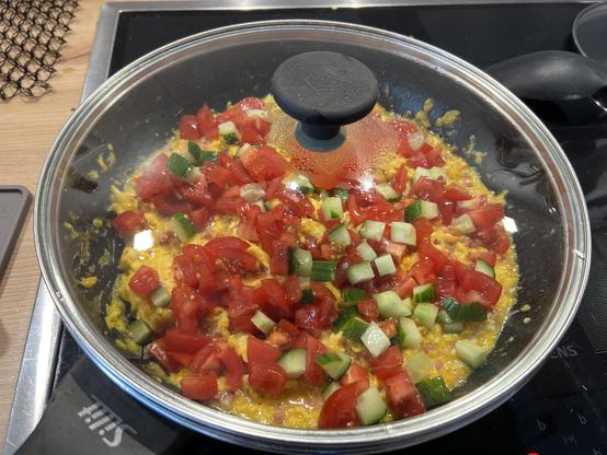 Eine große Pfanne Rührei mit Speckwürfeln, Tomaten und Gurken