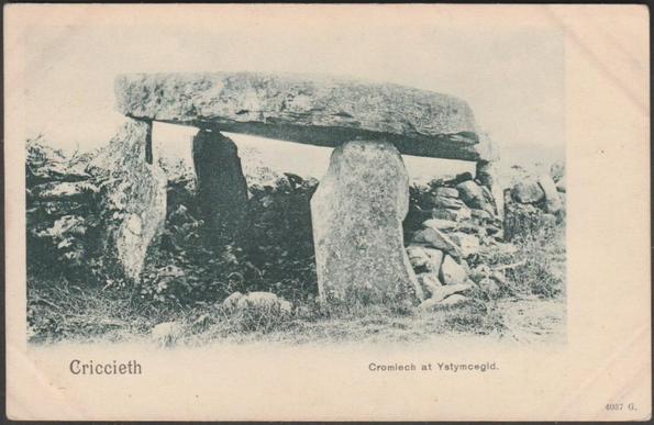 A printed vintage postcard showing the Ystum Cegid Isaf Dolmen or Coetan Arthur, a prehistoric chambered tomb near Garndolbenmaen by Criccieth in Sir Gaernarfon or Caernarvonshire. The dolmen sits within an old drystone wall which incorporates the monument. The capstone stands on top of four upright stones and is about 15 ft or 4½ m long.