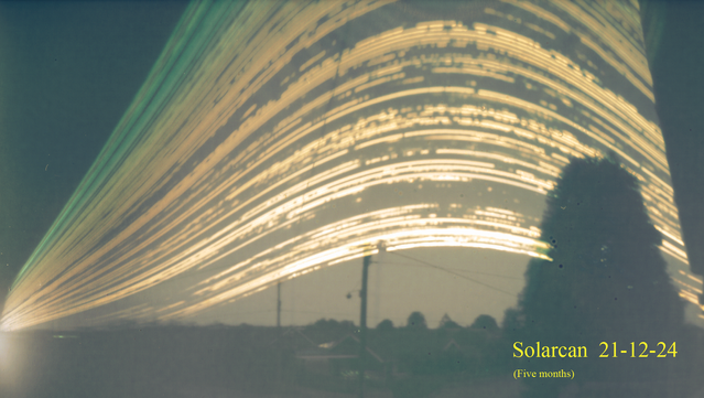 Showing the Sun's path through the sky over 5 months; tree in foreground to the right and a street with houses at the bottom.