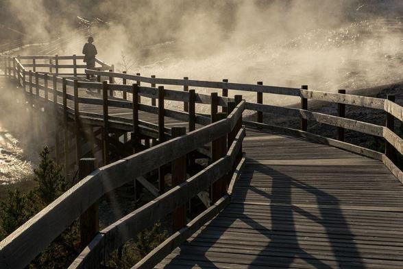 Woman standing on catwalk at Mammoth Hot Springs in Yellowstone National Park, with stream rising around her.