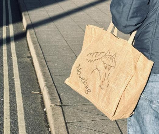 A person carrying a jute bag featuring a horse illustration and the word “Nosebag”.