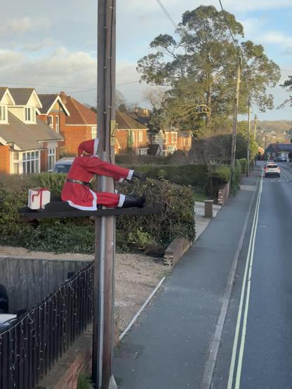 A Father Christmas decoration positioned by a road to look as though he’s crashed into a telegraph pole.