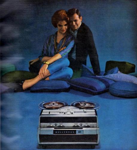 The foreground features a Wollensak 300 reel-to-reel tape recorder, prominently displayed on a blue surface. The background is a stylized, hazy blue backdrop with several blue cushions scattered across the floor, providing a relaxed and comfortable ambiance. The subtle smoke-like effect around the edges adds to the vintage feel of the image, perhaps suggesting a sense of nostalgia or a bygone era. The overall setting appears to be a home environment, possibly a living room.

A Caucasian couple, seemingly in their twenties or thirties, sit close together on the cushions. The woman, with short, reddish-brown hair, wears a stylish patterned shirt and blue pants. The man, with his dark hair neatly combed, is dressed in a dark sweater. They seem relaxed and content, possibly enjoying a moment of intimacy. The woman's subtle smile and the man's gentle gaze suggest a comfortable relationship. The image, likely from a vintage advertisement, showcases a scene of domestic leisure, highlighting the tape recorder as a central part of their enjoyment. The image likely captures the era when such devices were considered luxurious and were popular status symbols.