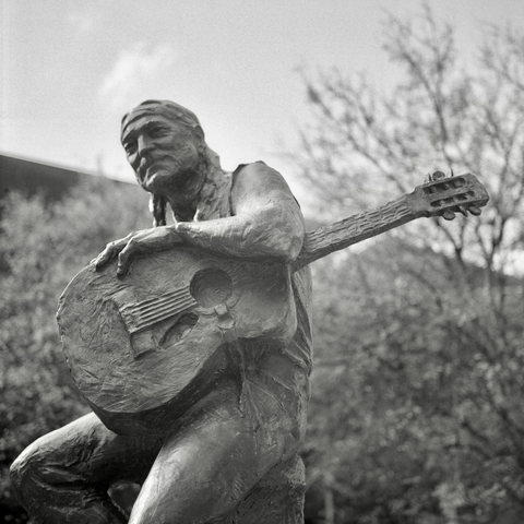A black and white film photo. The statue of Willie Nelson sits chill in downtown Austin, Texas. Tuesday, December 17, 2024. 