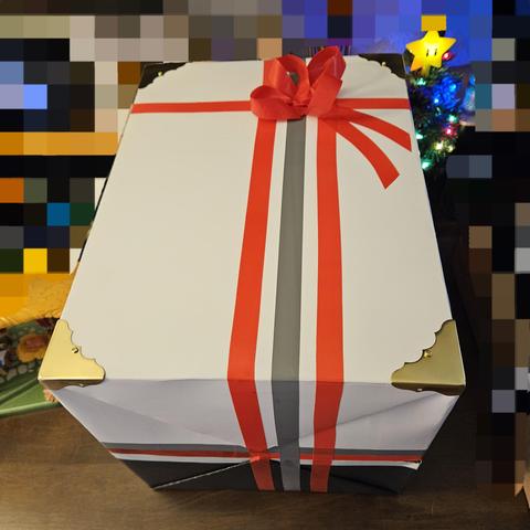 A gift is in focus, the background is colorful but mostly pixelated in a course manor. 
The gift is wrapped in black and white cardstock, black on bottom and white kn top half of the box. 
Vinyl electrical tape is used as stripping on all three axis. Joining the black and white, the stripping colors are grey on top, red in middle, and white on bottom, which contrasts with the black bottom paper color. 
The stripping splitting the box left to right are red left, a space, grey middle, a space, and red right. the spaces exposing their respective underpaper color. 
The stripping splitting front and back, which is about 75 percent to the back, is a single red strip, appearing much as a ribbon. Where these all converge on the top plane is a 4 looped vinyl tape ribbon flower, and 2 strips of tape cut at a sharp angle stick to the box to simulate loose ribbon ends. 
There are fancy store purchasex brass corner bumpers screwed to each of the top 4 box corners.