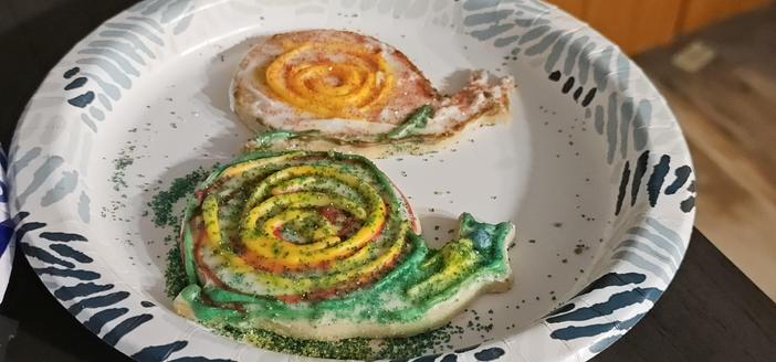 2 sugar cookies decorated with Christmas colors but both are shaped like snails