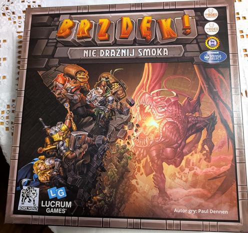 Pudełko z grą planszową Brzdęk, nie drażnij smoka.

Na rysunku jak sądzę czwórka poszukiwaczy skarbów w stylu jakby uciekli z rysunkowego fantasy i smok trochę jak T-Rex z ogniskiem w trzewiach równie dobrze mógłby grać w obcym :D