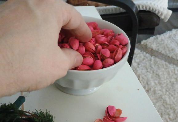 Fingers reach into a bowl of pink-dyed pistachios.