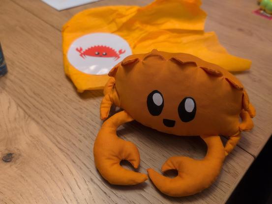 Ferris the crab standing on a table. Packaging paper with a Ferris sticker can be seen behind it.