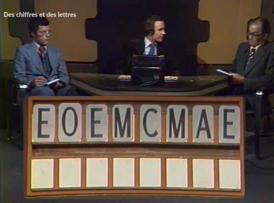Game show TV with two seated men in suits either side of a seated host. Very 70s fashion. In front of them is a wooden frame with alphabet letts on it. The two men have notepads and pen.