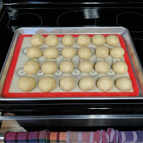 The dough divided into 24 equal weight pieces arranged on a silicone baking mat that is in a half sheet pan.