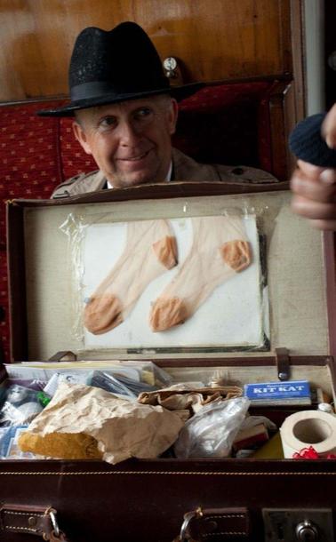 sell me stuff: A photograph of an old-fashioned smiling salesman wearing a black hat and sitting on a train. On his lap is a opened brown suitcase that contains a miscellaneous jumble of items, including stockings and a box of KitKats. Photo attribution: Flickr user dswilliams