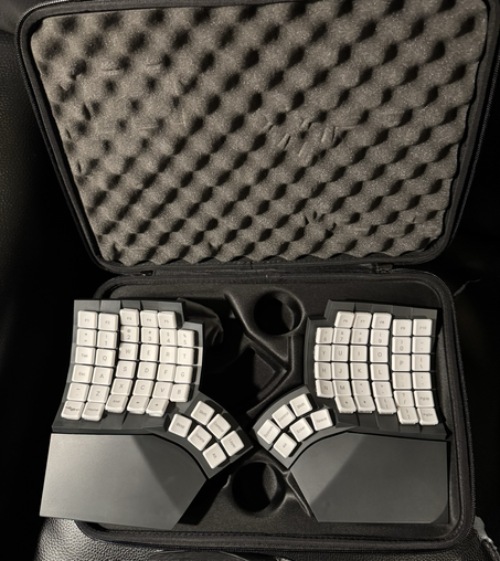 A photo of a black Moergo Glove80 split ergonomic keyboard with white keycaps.