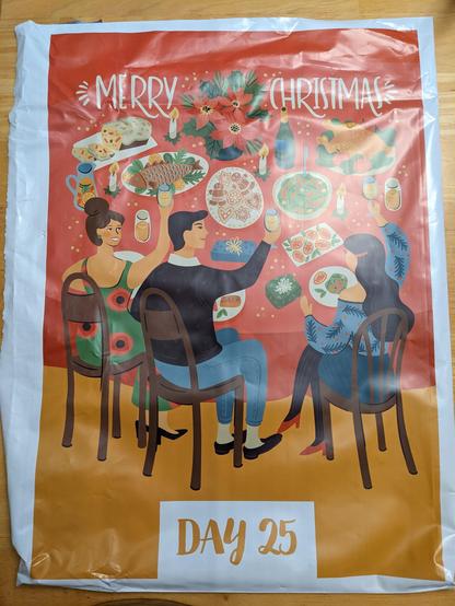 A large bag with Merry Christmas printed across the top. Below is are three people sitting at a Christmas table full of dinner. At the bottom, Day 25 is printed.