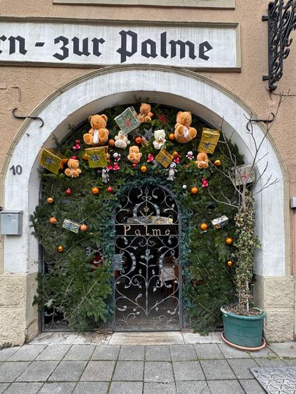 Ziseliertes Eisentürchen am zur “Palme” mit Tannengrün, Geschenken und Teddybären über dem Eingang