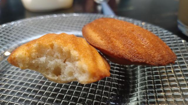 2 madeleines op glazen bordje, 1 met hap eruit waardoor je luchtige binnenkant ziet.