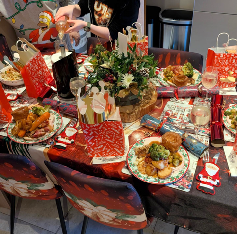 close up of our Christmas dinner table, with a floral centrepiece and the plates of Christmas dinner set and ready, with crackers, glasses of drink and gift bags by each place setting