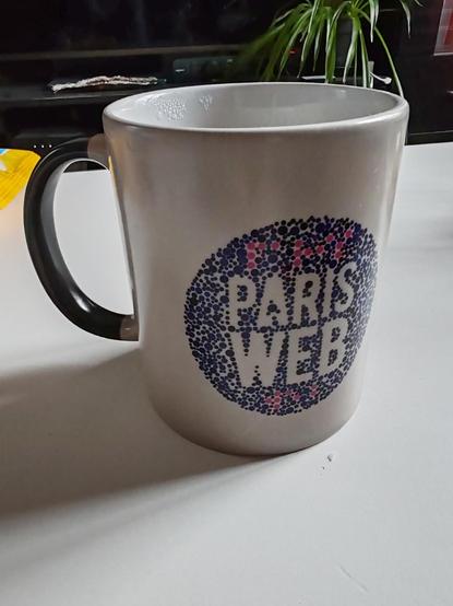 Thermo-reactive mug with Paris web logo like the Ishihara test with purple blue dots. It's also written in Braille in pink.