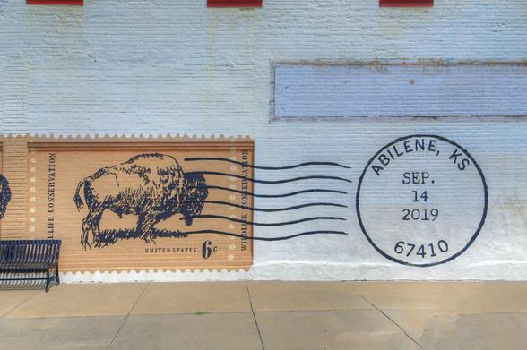 A mural on a brick wall resembles a large postage stamp featuring a bison, complete with cancellation marks