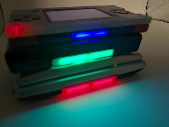 A gameboy macro sat on top of a ds lite and then sat on a ds phat with blue, green and red carts lite up respectively 