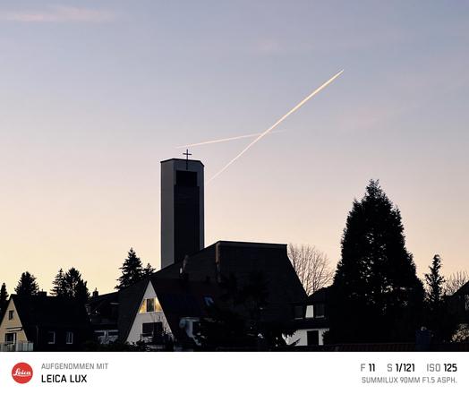 Kirchturm mit Kreuz im Sonnenuntergang. Neben dem Turm ein Kreuz von Kondensstreifen von Flugzeugen