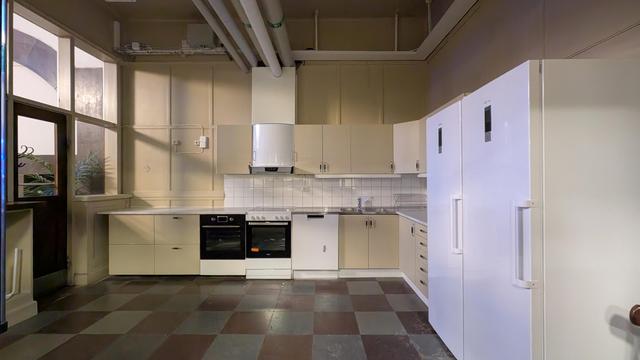 An empty kitchen in cream colours, two ovens, two large refrigerators, tubes at the ceiling