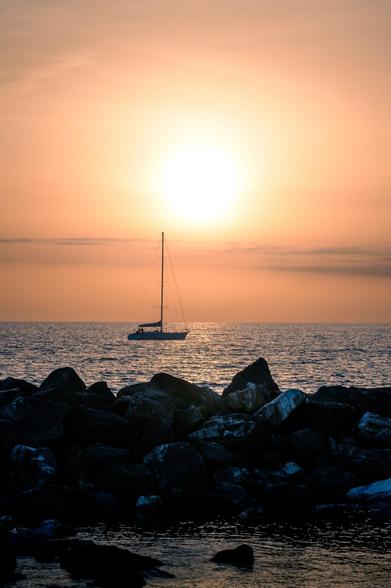 Boat in front of the setting sun in Pisa. Rocks in the foreground.