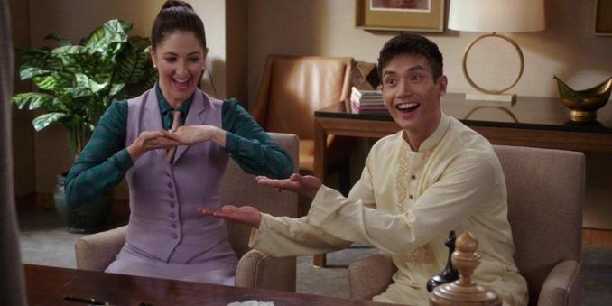 Still from the TV show "The Good Place," showing D'Arcy Carden as Janet seated next to Manny Jacinto as Jason Mendoza. Both of them are smiling very broadly.