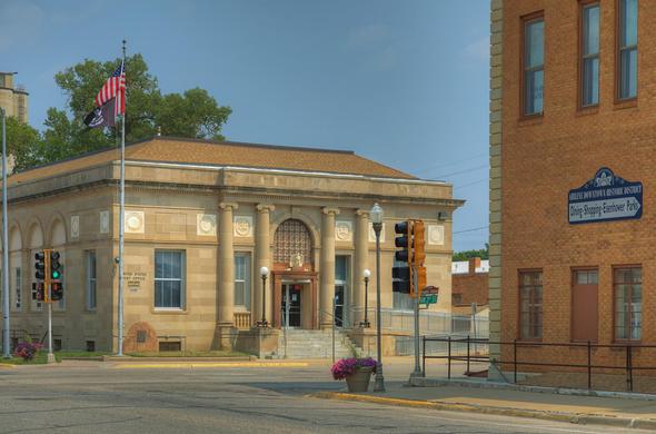 A historic post office with classical architectural elements stands at a street corner, displaying an American flag