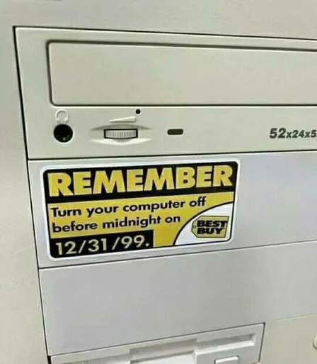 An old desktop computer tower with a "BEST BUY" sticker reminding the user to turn off their computer before midnight on 12/31/99, likely in reference to the Y2K bug.
